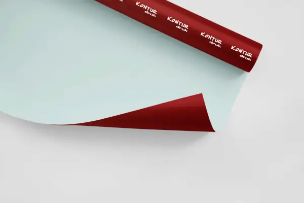 Rolka czerwonej folii samoprzylepnej z białym logo "KONTUR druk" na jasnoniebieskim tle.