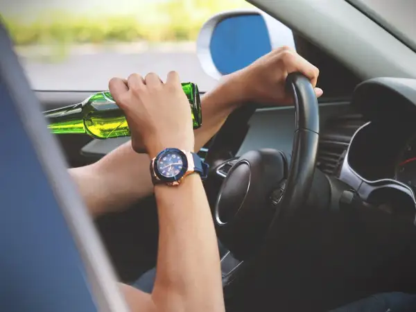 Ręce na kierownicy, jedna trzyma butelkę piwa. Ryzykowne zachowanie, stan po użyciu alkoholu.
