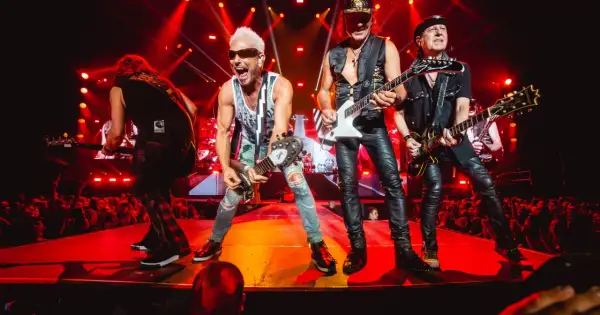 Zespół Scorpions na koncercie, grający swoje rockowe ballady. Wokalista z blond włosami i w okularach krzyczy do mikrofonu.