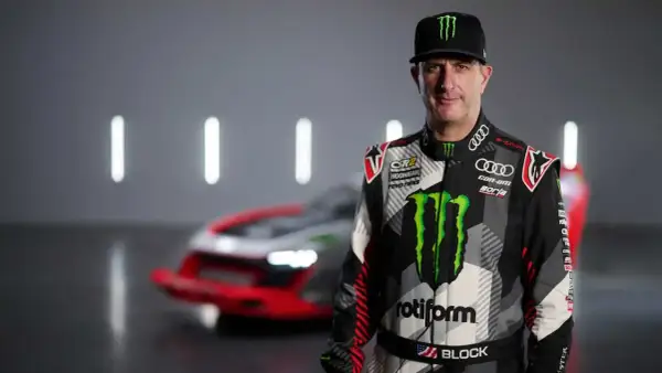 Ken Block, piloto de rally, posa con su traje de competición y un coche de Audi e-tron detrás.