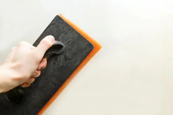Mano che impugna una spatola con spugna arancione per la pittura tamponato.