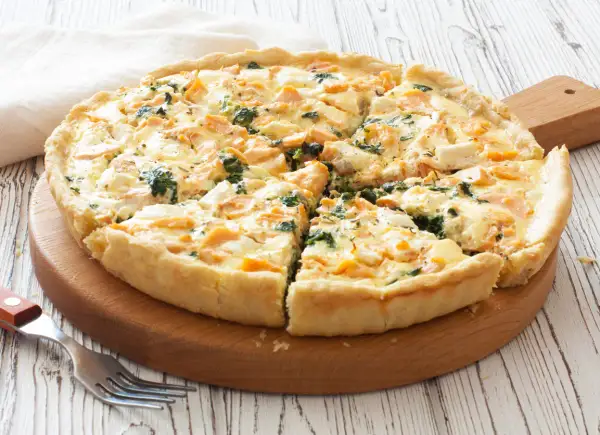 Pyszna tarta z łososiem, szpinakiem i serem feta, pokrojona na kawałki, na drewnianej desce.