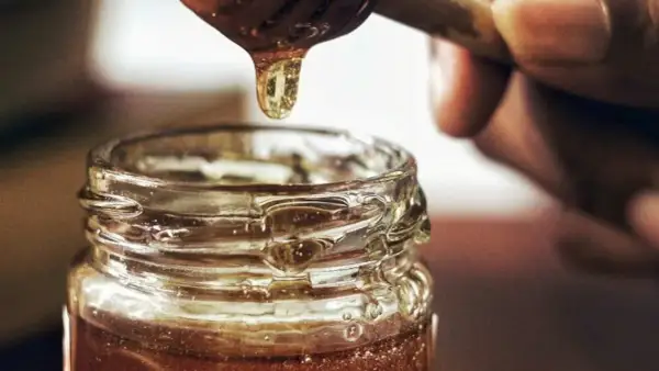 Goutte de miel doré tombant d'une cuillère dans un pot en verre. Une délicieuse alternative par quoi remplacer le sirop d'érable.