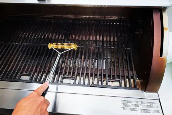En hand rengör gallret på en gasolgrill under tak med en grillborste.