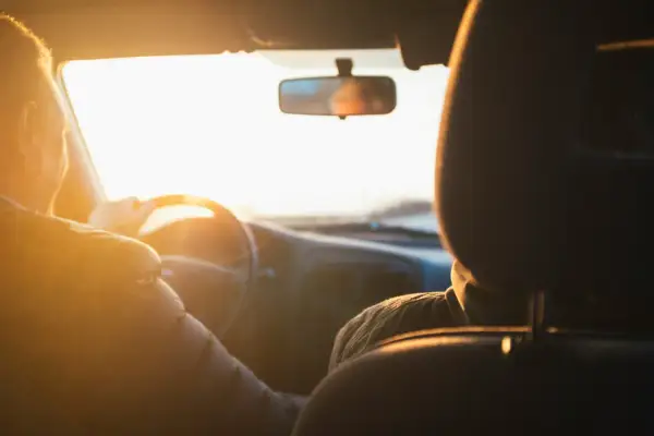 Två personer i en bil i solnedgången. Föraren håller i ratten. Vad betyder begagnad? Kanske bilen är begagnad, men resan är ny.