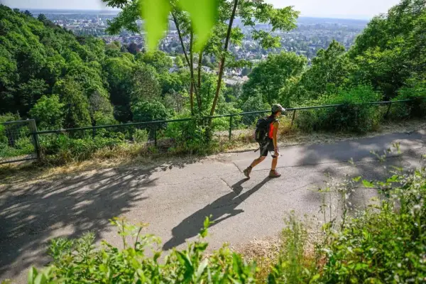 Persona con mochila camina por un sendero, disfrutando del senderismo y las vistas de la ciudad.