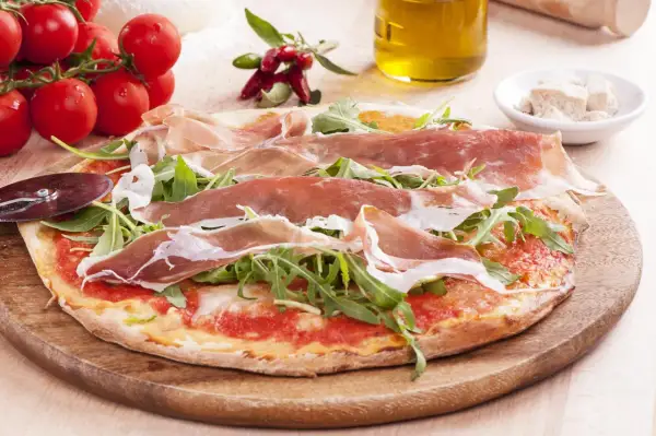 Pyszna pizza prosciutto z rukolą, pomidorami i oliwą z oliwek. Idealna na włoską ucztę.