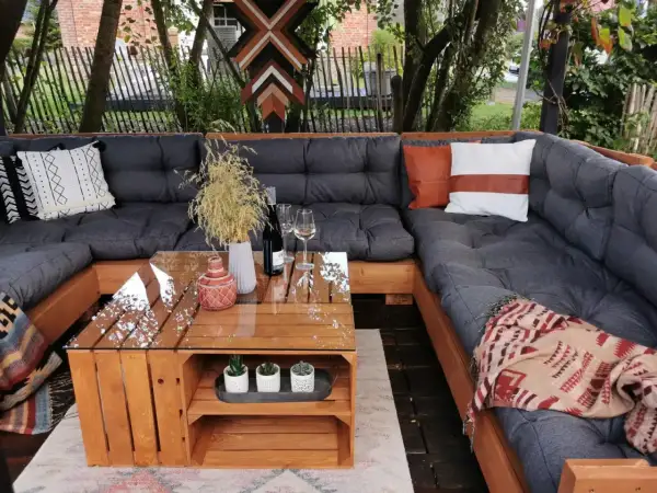 Gemütliches Palettensofa bauen: Eine Lounge-Ecke im Garten mit Glas-Couchtisch, Kissen und Decken. Perfekt für entspannte Stunden.
