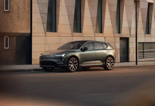 Elegante Volvo EX60 verde metallizzato parcheggiata davanti a un edificio moderno con facciata geometrica.