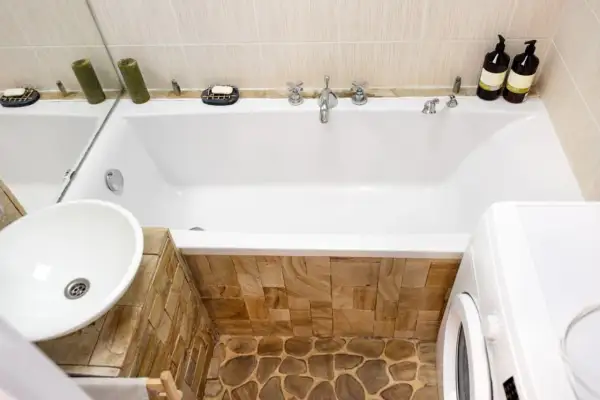 Badezimmer mit Waschbecken, Badewanne verkleiden mit Naturstein und Waschmaschine.