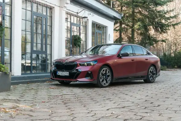 Elegancki, bordowy BMW 550e na brukowanym podjeździe przed nowoczesnym budynkiem.