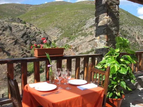Mesa puesta para comer en Patones de Arriba, con vistas a un valle montañoso. Flores y plantas decoran el balcón.