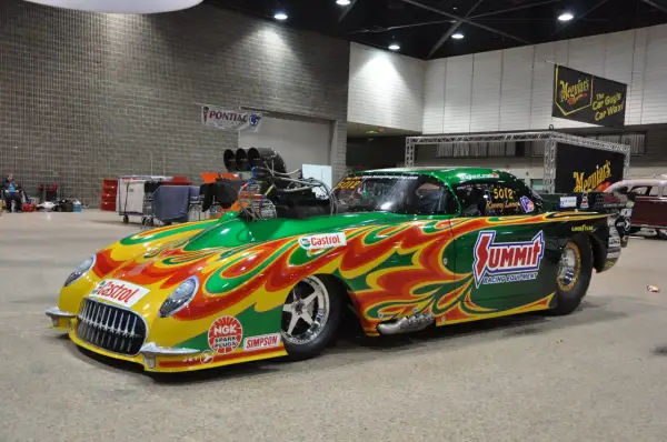 Une voiture de dragster aux couleurs vives, un exemple de tuning extrême, avec un moteur surdimensionné et des flammes peintes.