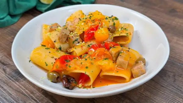 Paccheri con tonno fresco, pomodorini, olive e scorza di limone. Un piatto colorato e saporito, pronto per essere gustato.