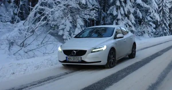 Białe Volvo V40 D3 pokonuje ośnieżoną drogę w lesie.