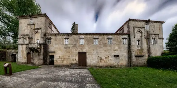 Las Torres de Allo, un edificio de piedra con un balcón ornamentado y ventanas blancas, se alza bajo un cielo nublado y dinámico.