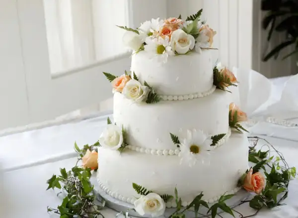 Elegancki tort weselny z białymi i brzoskwiniowymi różami, ozdobiony zielenią. Dowiedz się, jak zabezpieczyć kwiaty do tortu, by wyglądał pięknie.
