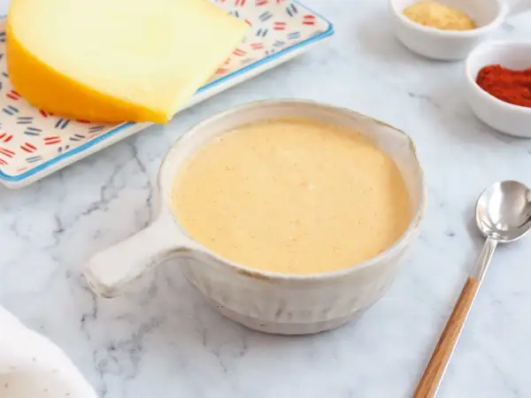 Crema de salsa de queso lista para servir, con un trozo de queso y especias al fondo.