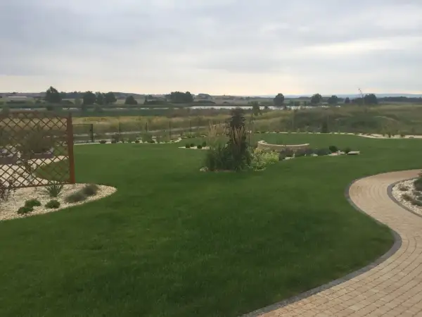Zadbany ogród z trawnikiem, kamiennymi ścieżkami i rabatami. W tle jezioro i pola. Fosforan monopotasowy pomógł uzyskać tak piękny, zielony trawnik.