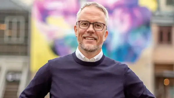 Niclas Hermansson ler glatt framför en färgglad väggmålning.