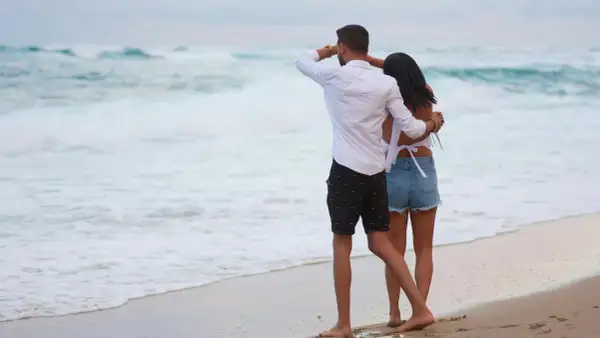 Ett par njuter av sin semester i Danmark vid havet. Mannen spanar ut mot vågorna medan kvinnan kramar om honom.