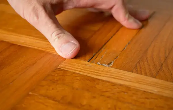 Dito come togliere la cera dal parquet verniciato: un dito indica una crepa sul legno lucido, mostrando il problema.