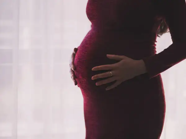 Ciężarna kobieta w czerwonej sukience obejmuje brzuch. Dylematy związane z umową zlecenie a ciążą.