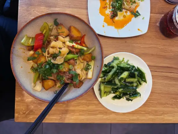 Ein Teller mit Nudeln, Kartoffeln und Gemüse, daneben ein Schälchen mit Gurkensalat. Typisch chinesisches Essen, das zum Genießen einlädt.