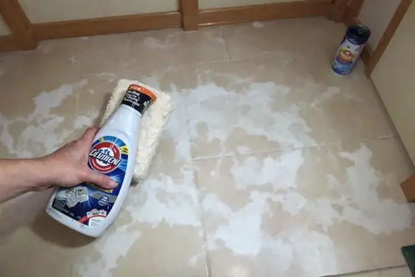 Main tenant nettoie carrelage neuf qui laisse un voile blanc avec un produit et une éponge.
