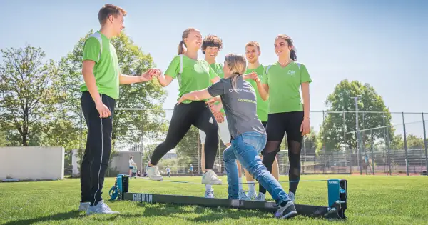 Junge Menschen üben auf einem Slackline-Parcours. Eine Dozentin unterstützt sie bei der physiotherapeutischen Ausbildung nebenberuflich.