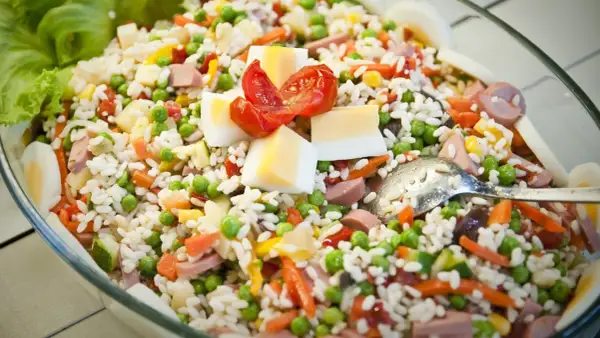 Insalata di riso ricca di ingredienti: piselli, carote, uova sode, pomodorini e salumi. Perfetta per un pasto fresco e completo.