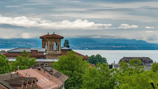 Widok na Jezioro Genewskie z dachu w Lozannie. W oddali góry, na pierwszym planie dachy i wieża.