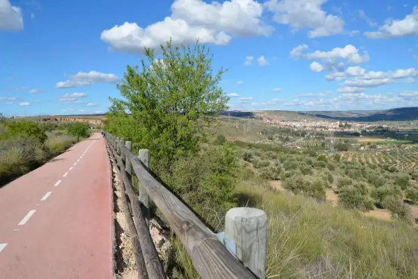 Un camino ciclista y peatonal, la **vía verde del Tajuña**, serpentea entre vegetación y un paisaje de olivos con un pueblo al fondo.