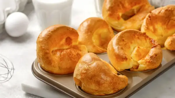 Goldbraune Yorkshire Pudding im Muffinblech, bereit für ein köstliches Rezept. Daneben ein Ei und ein Glas Milch.