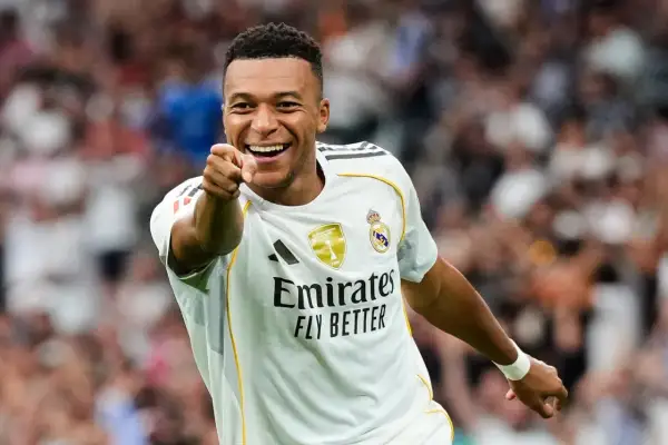 Uśmiechnięty piłkarz w białej koszulce Realu Madryt wskazuje palcem, jakby pytał: ile goli ma Mbappe?
