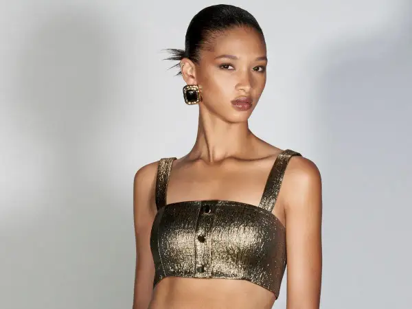 Modella con bronzer come si usa per un look radioso. Capelli raccolti, top dorato e orecchini neri.