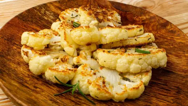 Tranches de chou-fleur entier au four, dorées et savoureuses, garnies de romarin frais sur une assiette en bois.