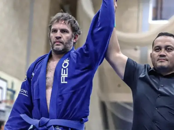 Tom Hardy i blå gi, med armen lyft som segrare i BJJ.