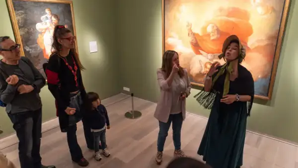 Un grupo de personas, incluyendo una niña, disfruta de una visita guiada en el **Día de los Museos Zaragoza**, admirando obras de arte.