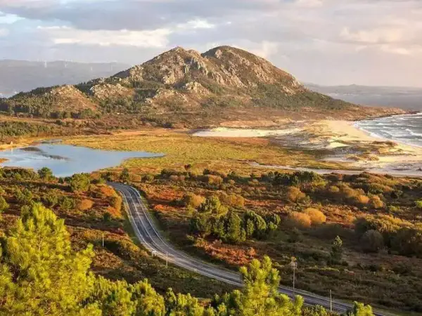 Carretera serpenteante hacia el monte Louro, con un lago, dunas y el mar al fondo.