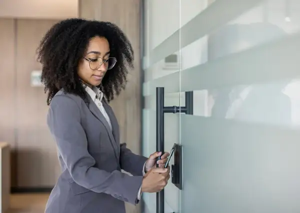 Donna con afro e occhiali usa lo smartphone per la rilevazione presenze, aprendo una porta in vetro.