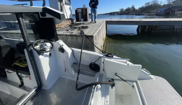 En vit båt vid en brygga. Vattnet är klart och man kan se alger i diesel-färgat vatten.