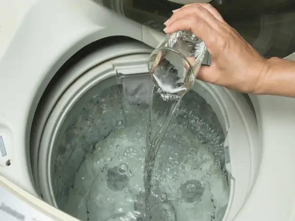 Mano versa liquido da un bicchiere nella lavatrice. Scopri quale aceto per lavatrice usare per un bucato impeccabile.
