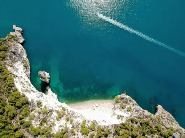 Vista aerea della cala della pipa, con scogliere bianche, vegetazione verde e mare turchese. Una barca lascia una scia sull'acqua.
