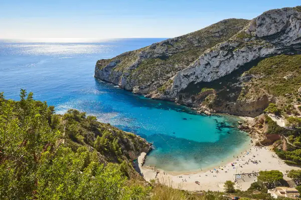 Bahía de aguas turquesas y arena dorada, rodeada de acantilados verdes. Un paraíso de playas bonitas con gente disfrutando del sol.