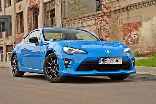 Niebieskie coupe Toyota GR86 z czarnymi felgami stoi przed zniszczoną ceglaną ścianą.