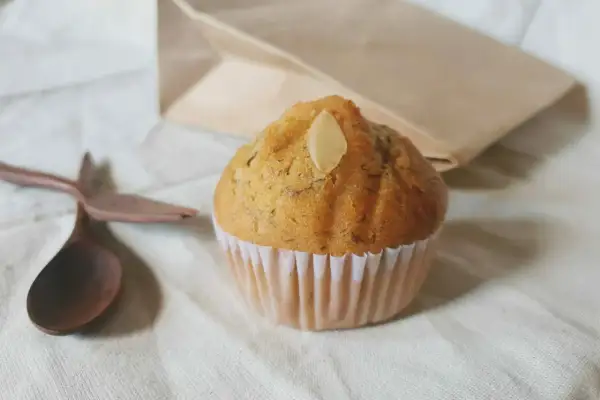 Un soffice muffin allo yogurt, guarnito con una mandorla, pronto per essere gustato con un cucchiaio di legno.