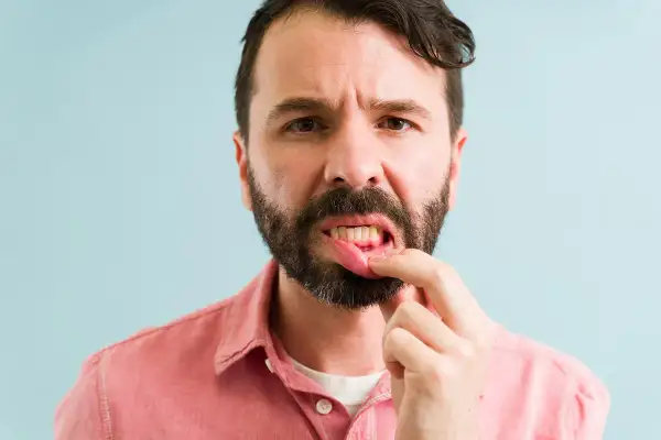 Hombre preocupado se toca la boca, mostrando encias sangrantes.
