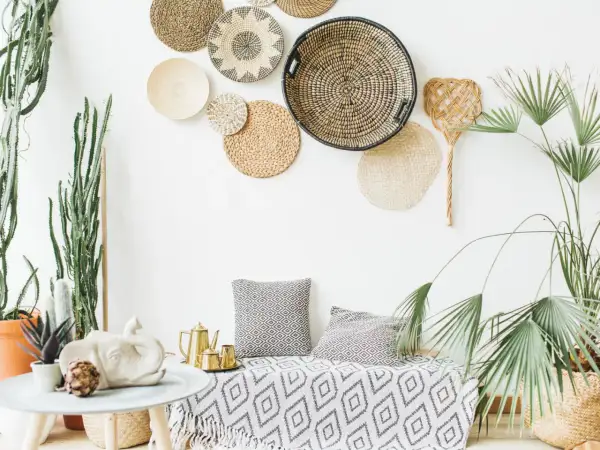 Wnętrze w stylu boho chic: plecione kosze na ścianie, sukulenty, złoty czajniczek i poduszki z geometrycznym wzorem.