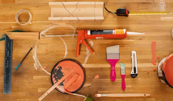 Pistolet à mastic, rouleau, pinceaux et pot de peinture orange sur un établi en bois.
